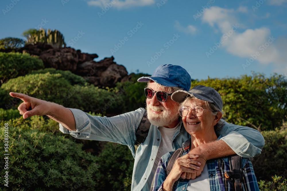 Smiling old senior couple enjoying outdoor excursion in mountain environment. Beautiful active elderly people having healthy lifestyle in a trekking day