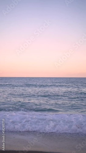 A vertical video of a waves crashing on the golden sandy beach during sunset