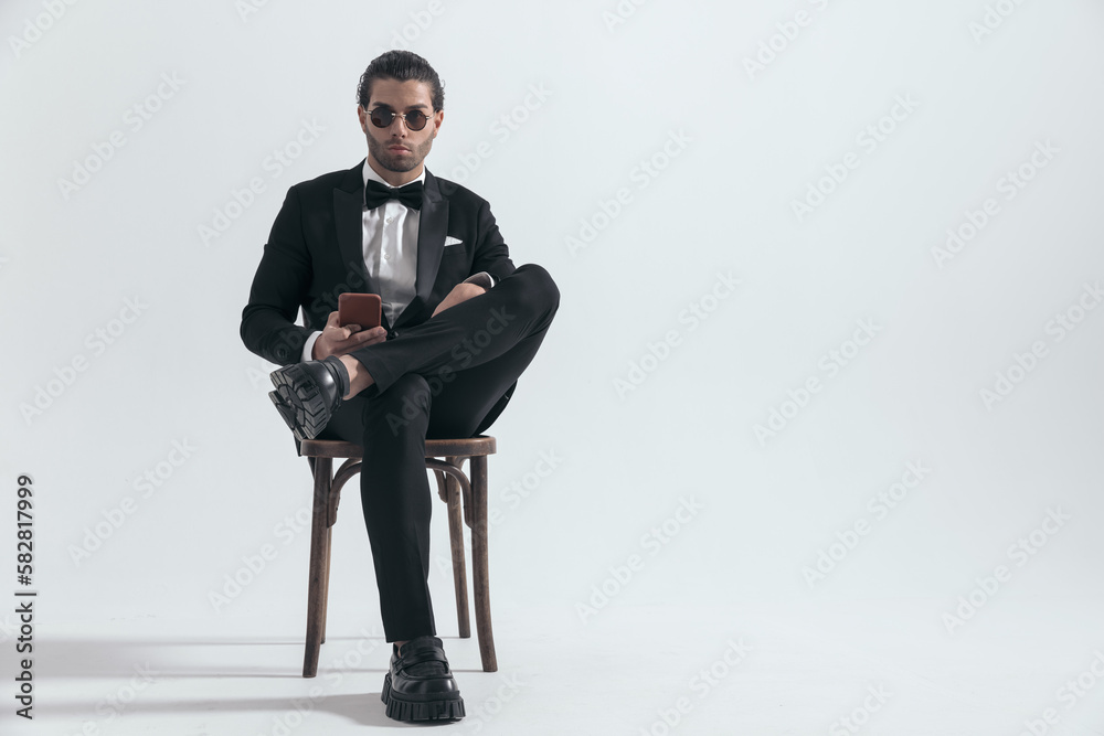 confident businessman in black tuxedo holding mobile and texting confident businessman in black tuxedo holding mobile and texting