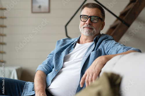 Happy mature man sitting on couch. Portrait of man relaxing at home with big smile.