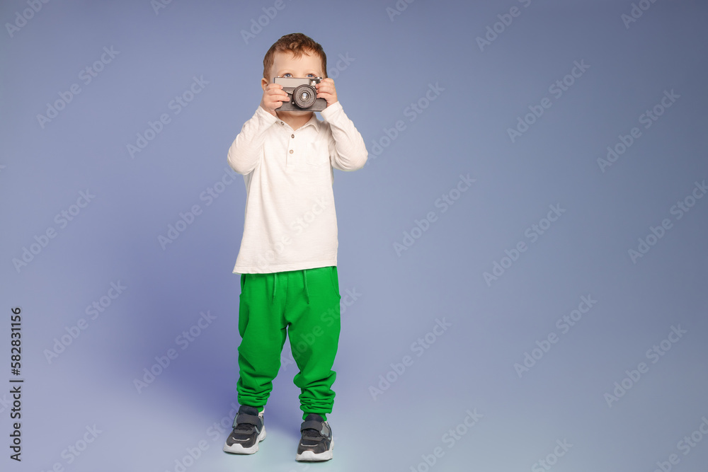 One young male child taking a picture with retro camera and looking at the subject on blue background One young male child taking a picture with retro camera and looking at the subject on blue background