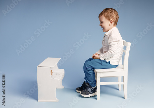 Young male pupil sitting on white chair and excited to learn piano photo