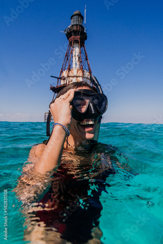 Cheerful, joyful, young athletic woman, snorkeling and swimming on beach vacation, having fun in the tropical water, with a big toothy smile, laughing, enjoying her honeymoon with lighthouse