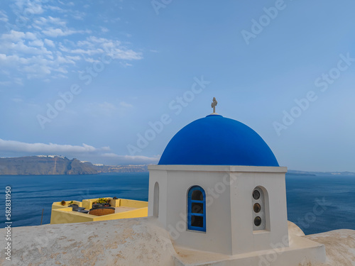 White church dome with blue roof in Oia, Santorini island with a sea view in background
