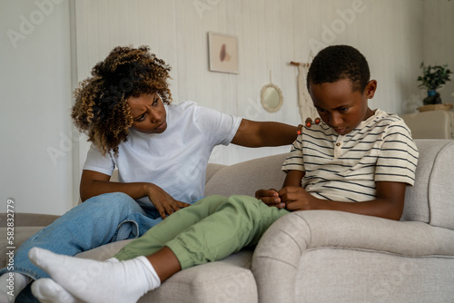 Frowning single African American mother scolding naughty boy sitting on sofa at home. Misbehaviour of children. Annoyed angry mixed race woman think about punishment for mischievous spoiled ignore son