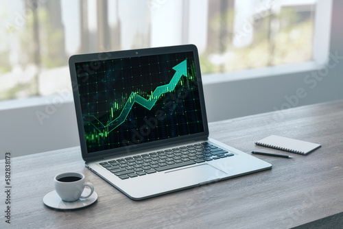 Close up of laptop on office desktop with coffee cup, notepad and growing green candlestick arrow on blurry background with window and city. Financial growth, market and trade concept. 3D Rendering.