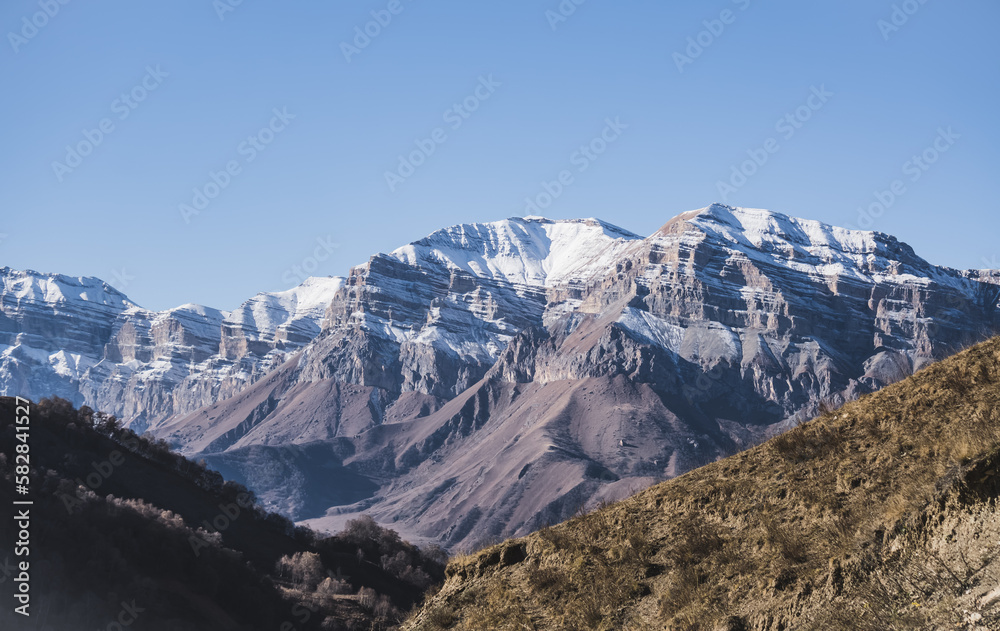 Panorama of a mountain range from layers of rocks with the first snow on the rocks and slopes, autumn mountains with the first snow