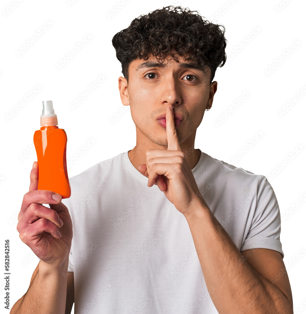 A young latin man holding a solar protection cream keeping a secret or asking for silence. A young latin man holding a solar protection cream keeping a secret or asking for silence.