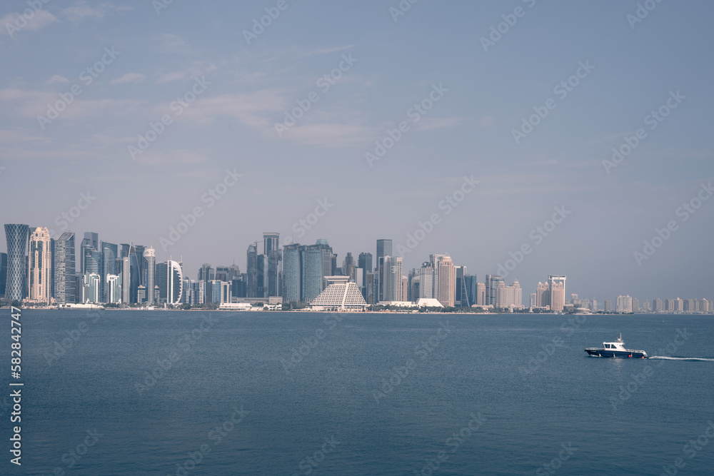 doha skyline at day, skyscrapers standing tall and in line in the concrete jungle, and the small boat passing the gulf