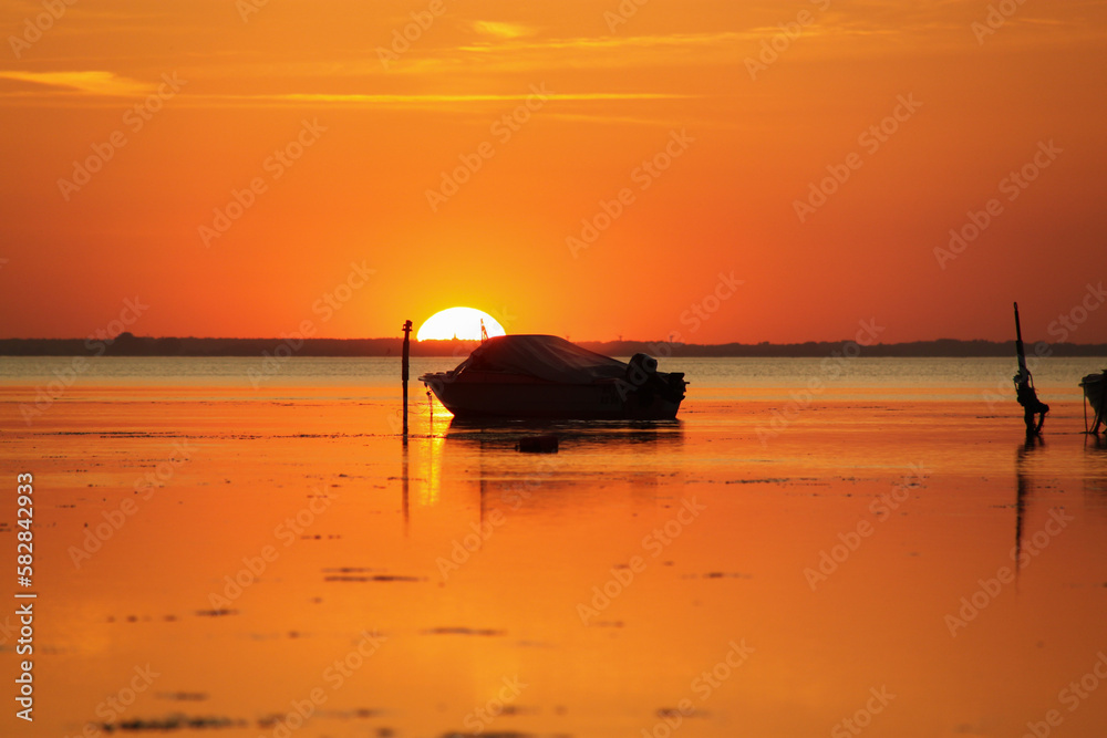 Silhouette of a motor vessel on calm baltic sea during golden sunset. Boat tied to a pole, close to the beach of Greifswald, Germany Silhouette of a motor vessel on calm baltic sea during golden sunset. Boat tied to a pole, close to the beach of Greifswald, Germany