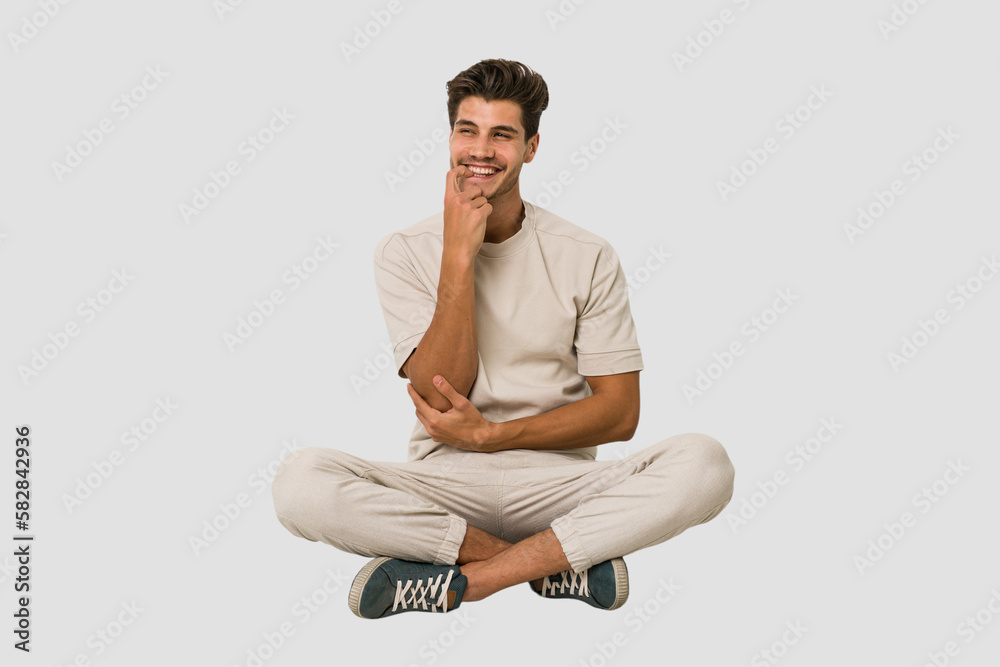 Young caucasian man sitting on the floor isolated on white background relaxed thinking about something looking at a copy space. Young caucasian man sitting on the floor isolated on white background relaxed thinking about something looking at a copy space.