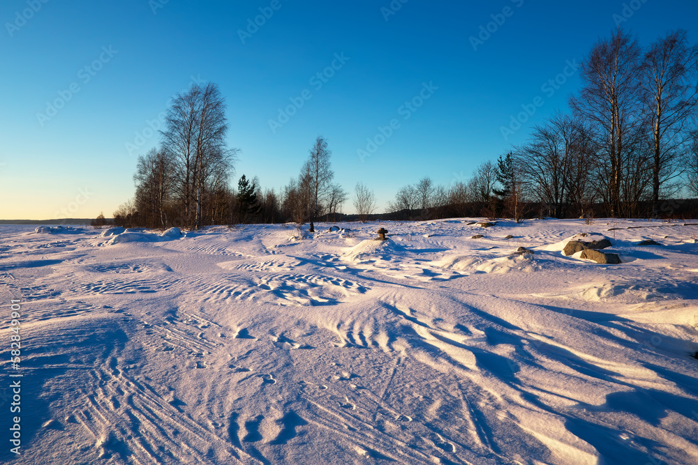 View of the snow-covered frozen lake at sunset. Winter landscape. Lake shore with trees View of the snow-covered frozen lake at sunset. Winter landscape. Lake shore with trees