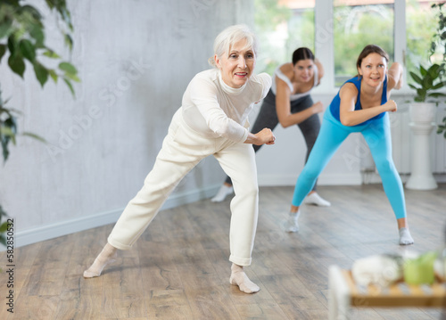 Cheerful sporty senior woman training movements of rhythmic latin zumba with group in fitness studio. Concept of active lifestyle of aged adults