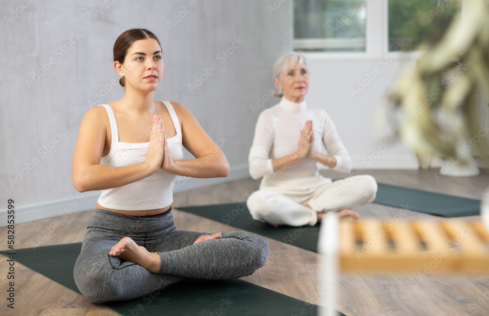 Elderly young women sitting on mats in Lotus Position Padmasana during yoga stretch joint workout in fitness center