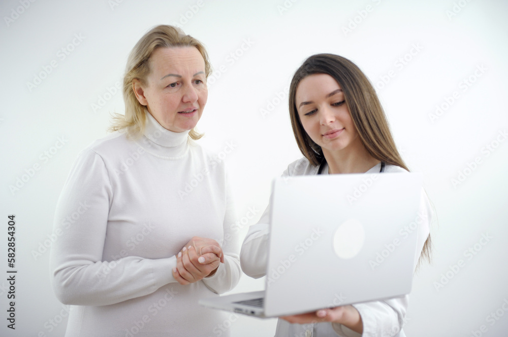 young girl doctor shows tests on laptop to an adult woman in white clothes on a white background advertising a good medicine helping patients care internet consultation online hospital polyclinic young girl doctor shows tests on laptop to an adult woman in white clothes on a white background advertising a good medicine helping patients care internet consultation online hospital polyclinic