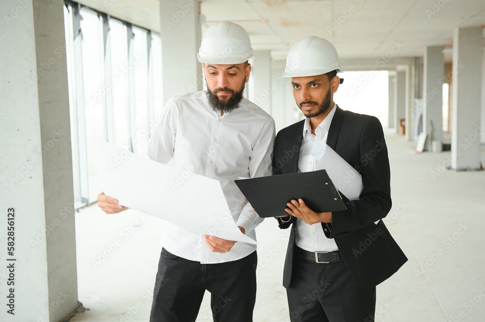 Multiracial male coworkers in hardhats discussing project on construction site Multiracial male coworkers in hardhats discussing project on construction site