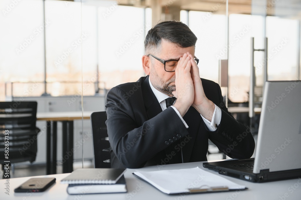 Tired stressed office worker sitting at desk and thinking, he is rubbing his eyes and feeling exhausted. Tired stressed office worker sitting at desk and thinking, he is rubbing his eyes and feeling exhausted.