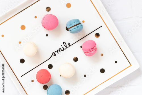 Small pastel colored macaroons on a square minimal style table in flat lay top view image. Delicious macaroon desserts with a smile texted plate.
