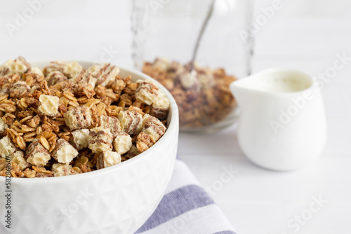 Home made breakfast bowl with granola, muesli and milk. White toned image of a delicious breakfast plate with cereal jar in the background.