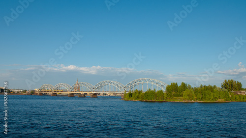 RIGA, LATVIA-JUNE 5, 2021:in the photo, a railway bridge, a river in the foreground, blue sky and clouds in the background