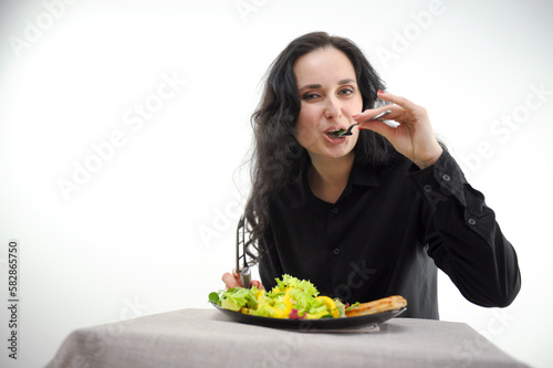 Fotografija on white background woman in black clothes eats a salad and meat with fork looks