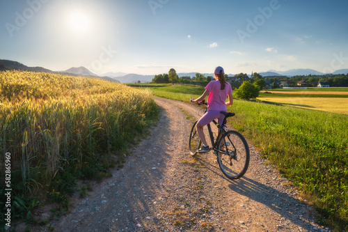 Woman on mountain bike on gravel road at sunset in summer