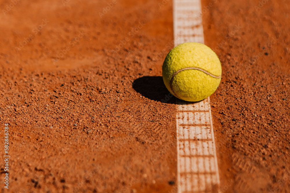 Light orange empty outdoor clay court surface dry grungy ground baseline detail for playing tennis with net in sunny day with yellow green ball, gravel texture background, copy space for text 

