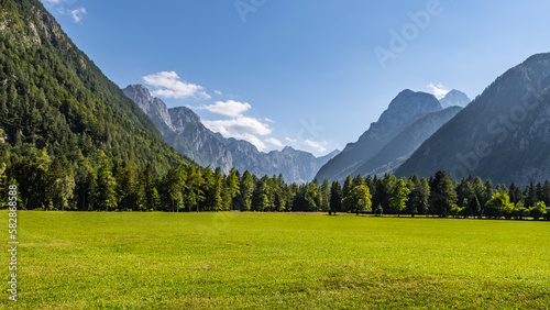 View of the Krma Valley on a sunny summer day. Grassy green pastures in the foreground and breathtaking peaks of the Julian Alps on background. Triglav National Park, Slovenia
