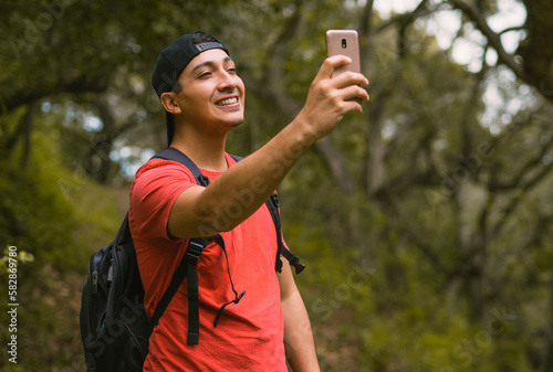 young man takes a selfie while hiking in garland ranch regional park, california, dressed in red with a cap. 