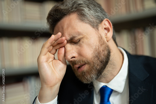 Close up portrait of stressed man with headache migraine. Tired businessman is working overtime and has headache. Man with laptop at workplace, suffers from headache. Migraine from overwork.