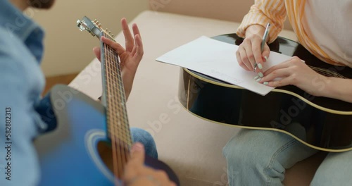 teacher,tutor playing guitar while student writing on exercises book, close up cropped video. slow motion,female guitarist making notes in notebook with pen.Music composers thinking about text photo