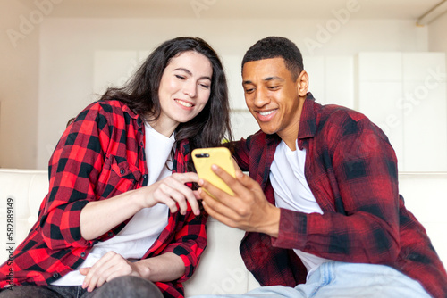 Cuadro en lienzo young multiracial couple using smartphone at home on comfortable sofa, african a