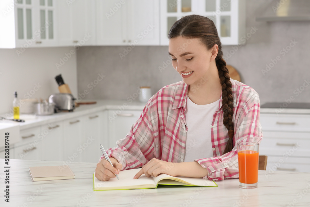 Beautiful young woman writing in notebook at white marble table indoors Beautiful young woman writing in notebook at white marble table indoors