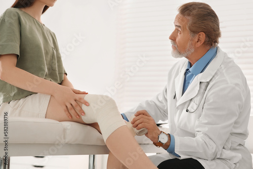 Orthopedist applying bandage onto patient s knee in clinic
