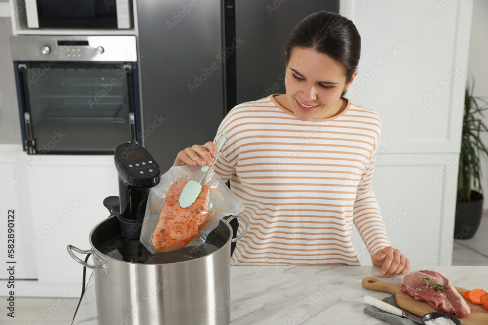 Woman putting vacuum packed meat into pot with sous vide cooker in kitchen.  Thermal immersion circulator foto de Stock | Adobe Stock