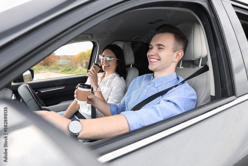 Happy young couple with cups of coffee in car