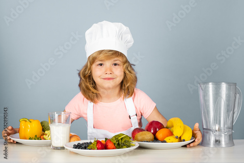 Portrait of chef child in cook hat. Cooking at home, kid boy preparing food from vegetable and fruits. Healthy eating.