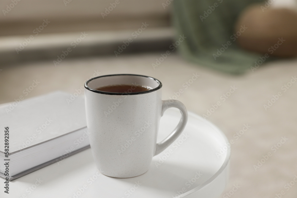 Ceramic mug of tea and book on white table indoors. Mockup for design