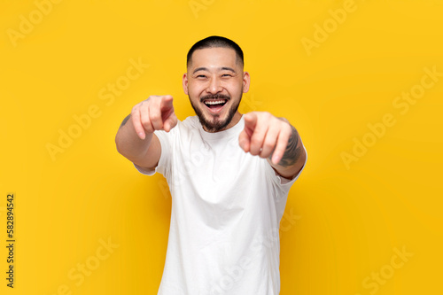 Photos adult tattooed asian man in white t-shirt mocks and jokes on yellow isolated bac