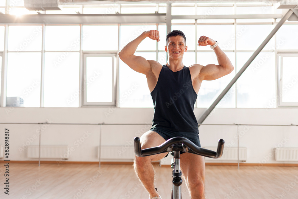 Fototapeta premium athletic male cyclist trains on exercise bike in bright room, guy in sportswear sits on simulator in fitness room