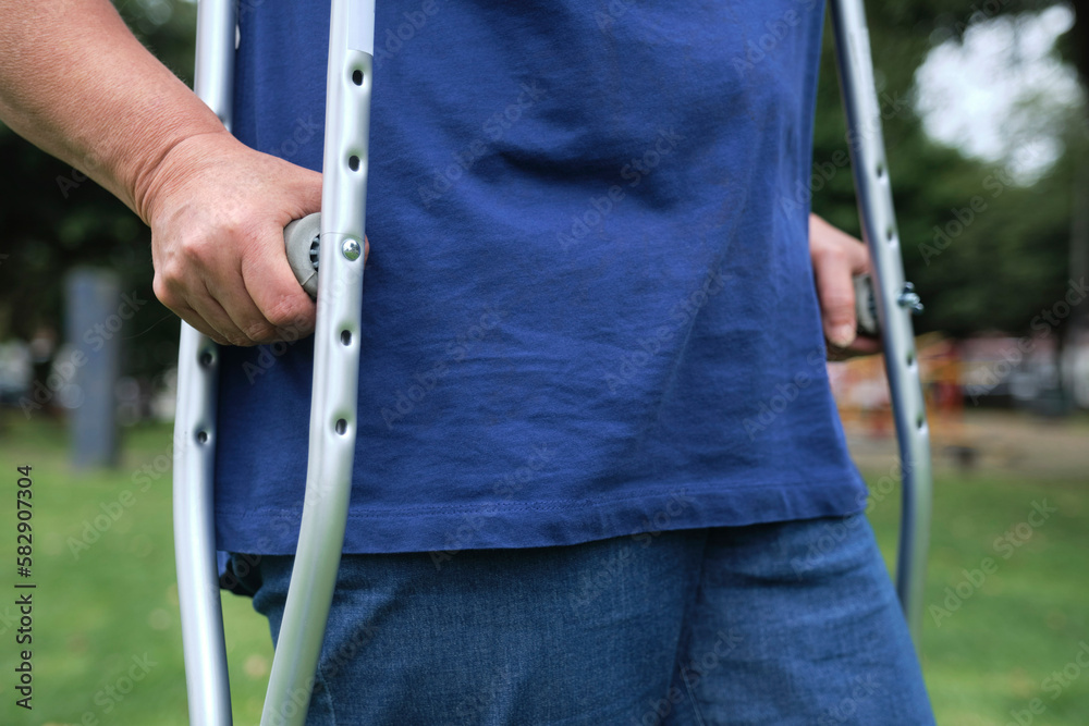 Unrecognizable woman walking outdoors with the help of crutches in the process of physical rehabilitation after an injury, detail of the hands. Unrecognizable woman walking outdoors with the help of crutches in the process of physical rehabilitation after an injury, detail of the hands.