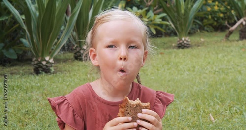 Cute little girl eating a slice of banana muffin outdoors.