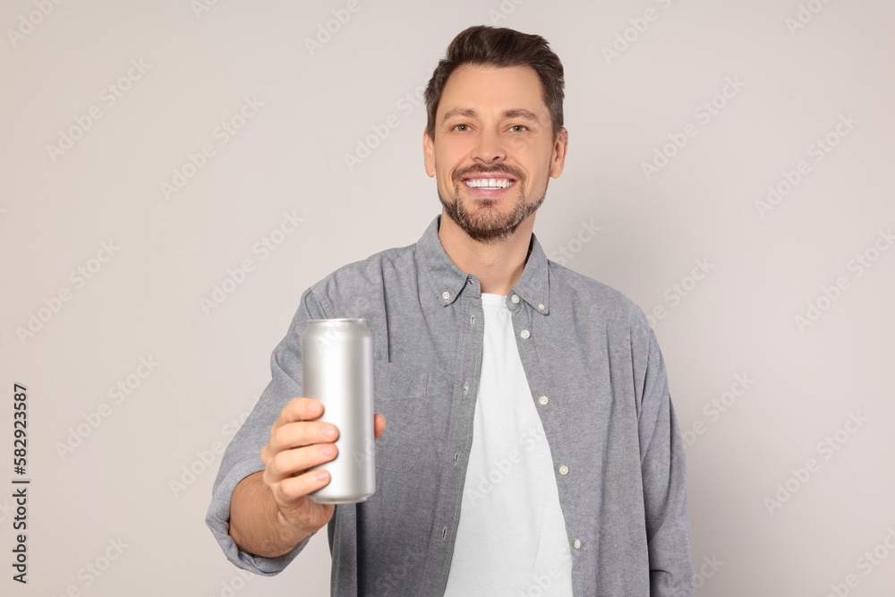 Happy man holding tin can with beverage on light grey background Happy man holding tin can with beverage on light grey background
