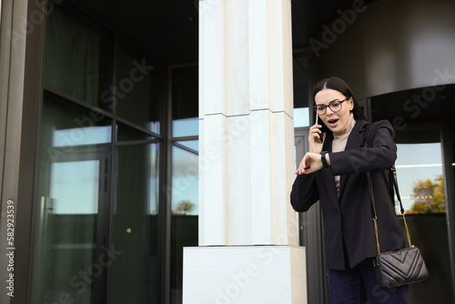 Emotional woman checking time while talking on smartphone outdoors. Being late concept