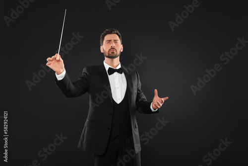 Professional conductor with baton on black background