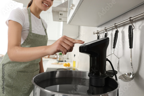 Fototapeta Naklejka Na Ścianę i Meble -  Woman using thermal immersion circulator in kitchen, closeup. Sous vide cooking
