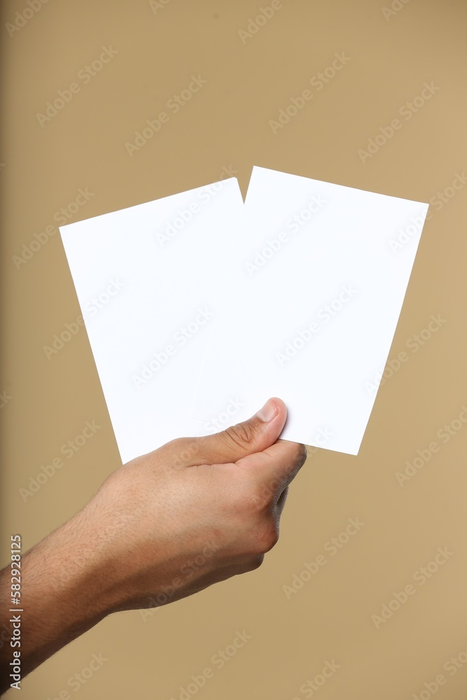 Man holding sheets of paper on beige background, closeup. Mockup for design Man holding sheets of paper on beige background, closeup. Mockup for design