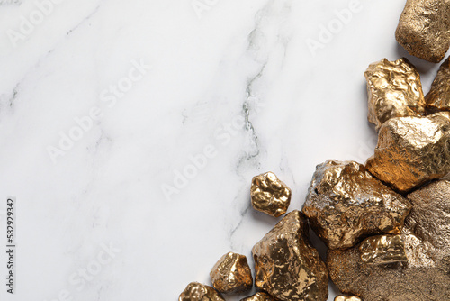 Pile of shiny gold nuggets on white marble table, flat lay. Space for text