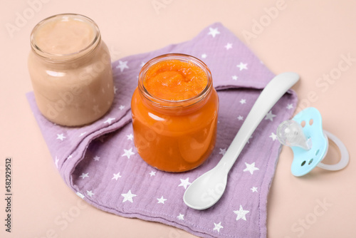 Healthy baby food, spoon and pacifier on pale pink background