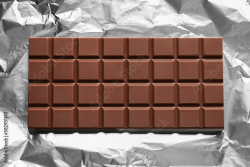 Delicious milk chocolate bar on foil, top view